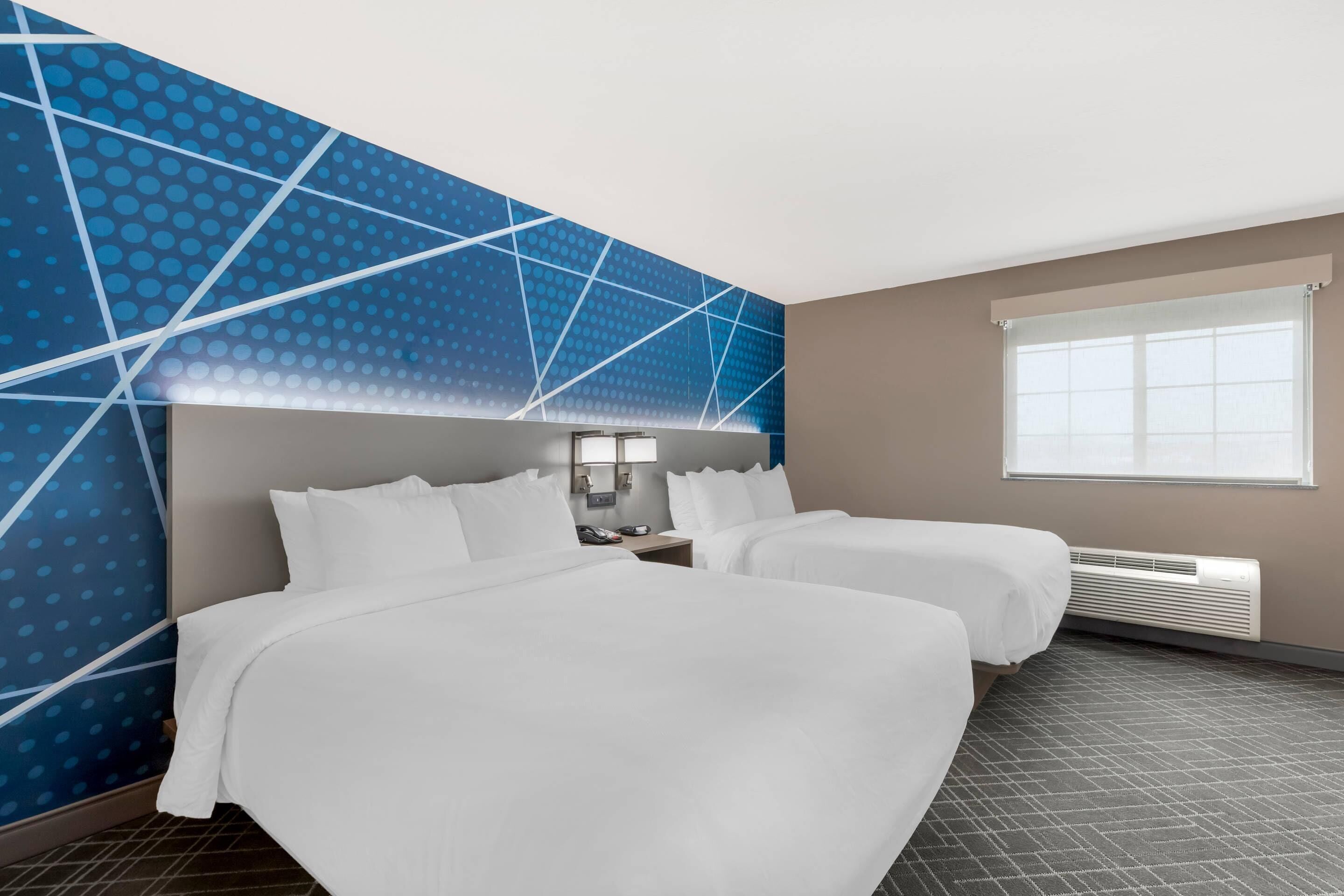 Ein Hotelzimmer mit zwei Betten, einem großen Fenster und einer Wand mit blauem Muster.