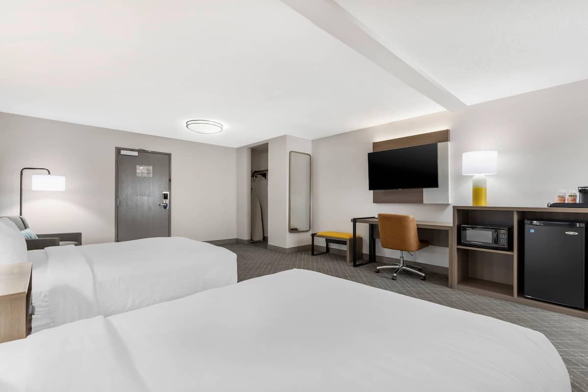 Une chambre d’hôtel avec deux lits, un bureau avec une chaise, une télévision, un four à micro-ondes et un réfrigérateur.