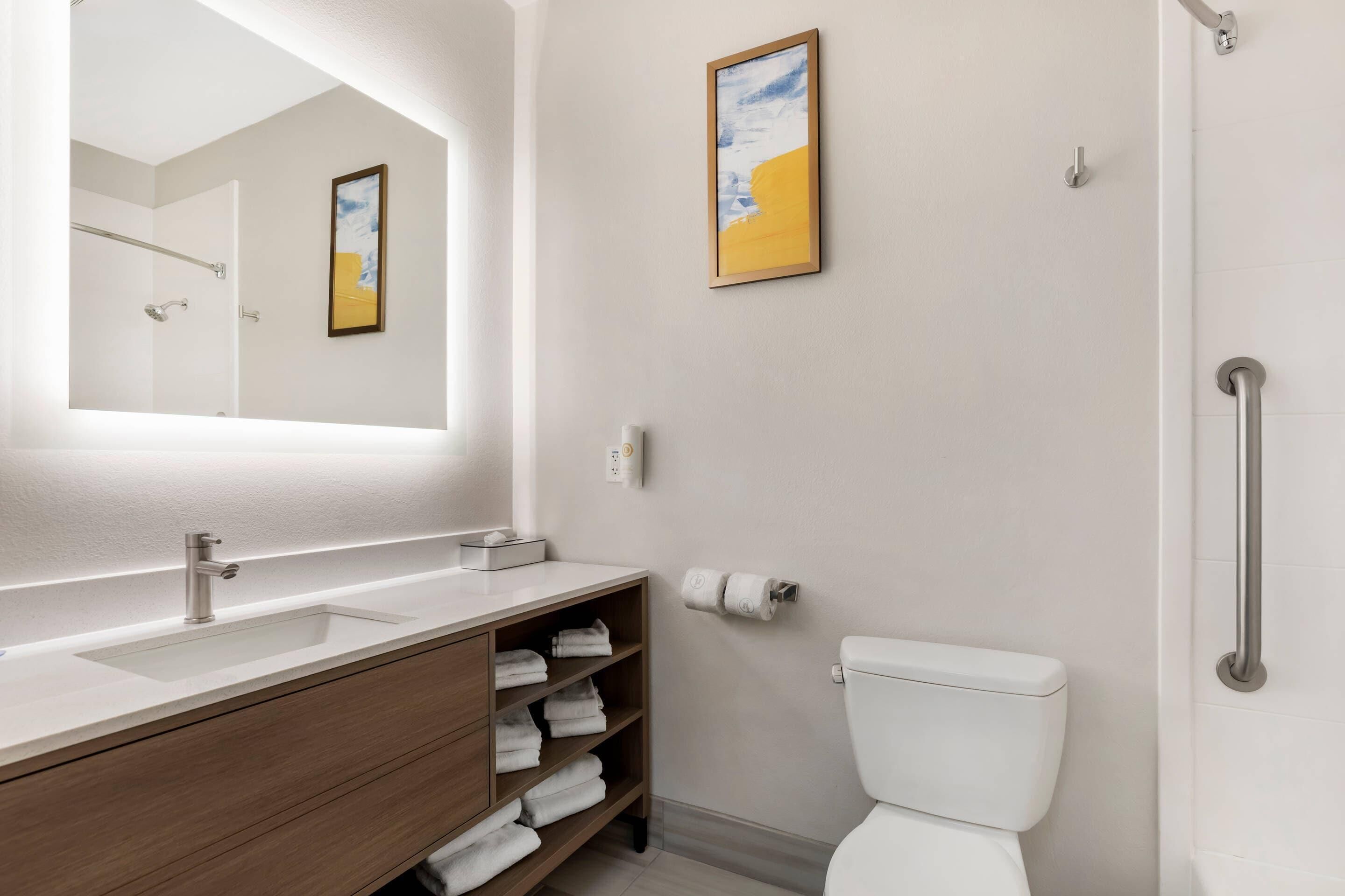 Ein modernes Badezimmer mit einem großen Spiegel, einem Waschbecken mit Holzschrank, einer Toilette und einer Duschkabine.