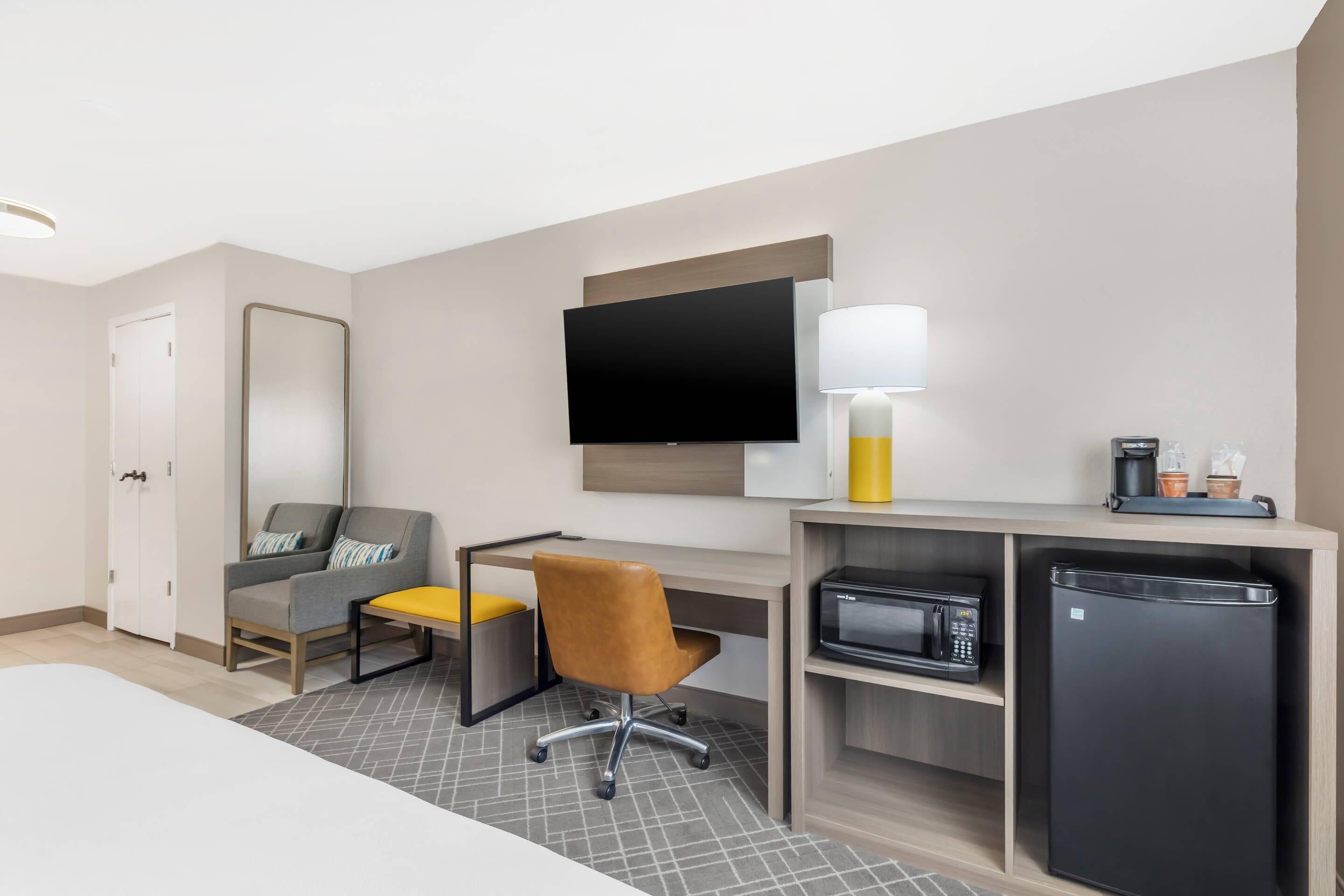 Habitación de hotel con cama, escritorio con silla, televisor de pantalla plana, lámpara, microondas y refrigerador.