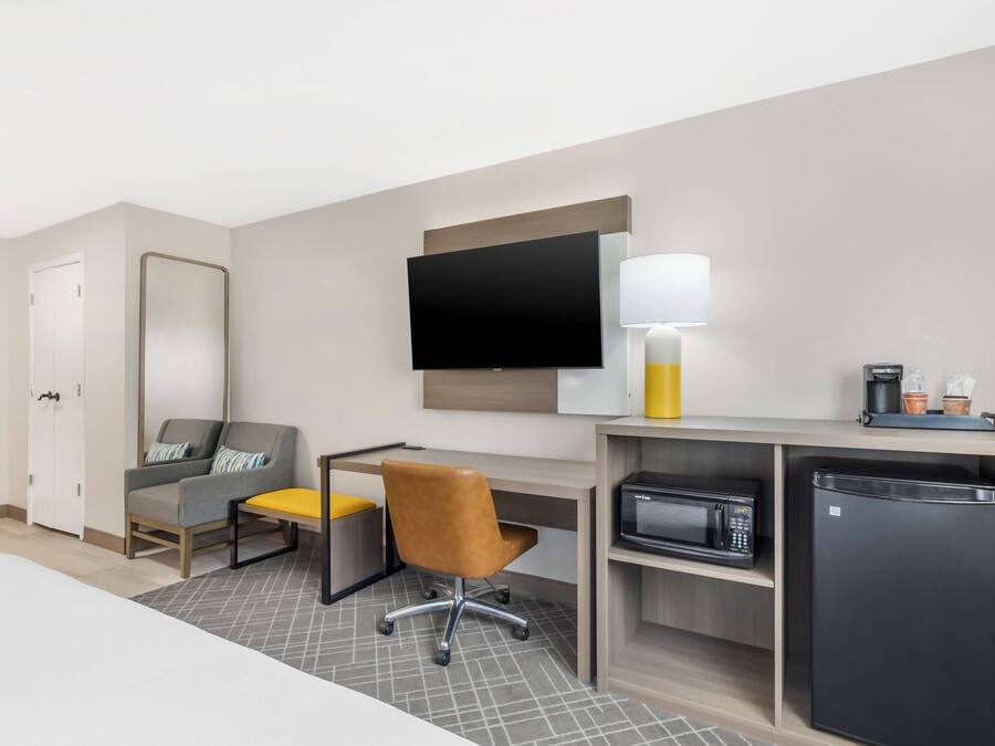 Habitación de hotel con cama, escritorio con silla, televisor de pantalla plana, lámpara, microondas y refrigerador.