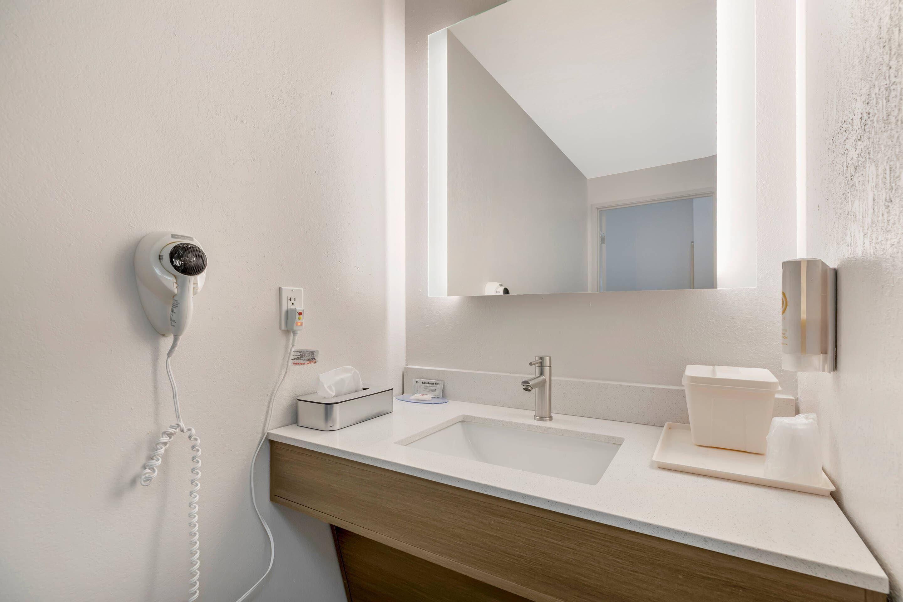 Un baño moderno con lavamanos blanco, un espejo, un secador de pelo y una caja de pañuelos.