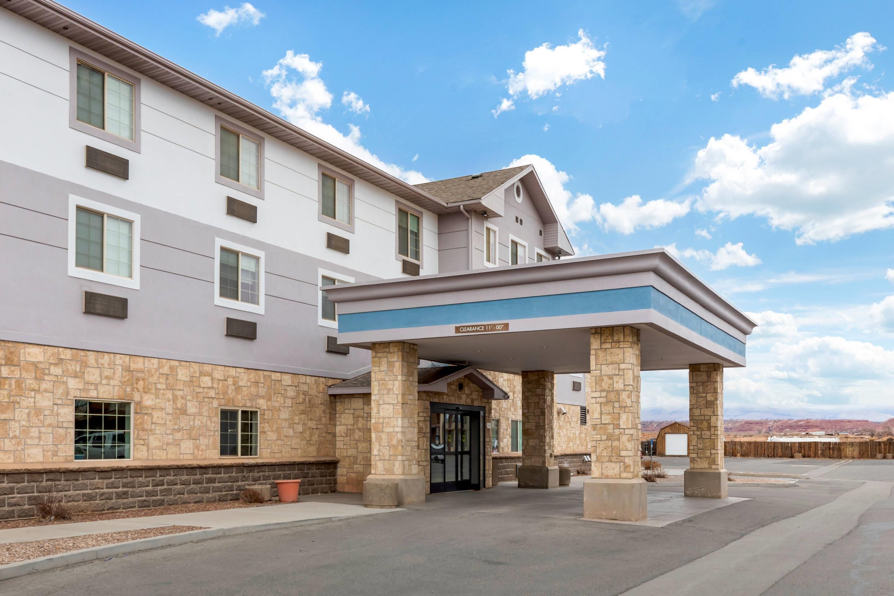 A multi-story hotel with a stone facade, a covered entrance, and a clear sky.