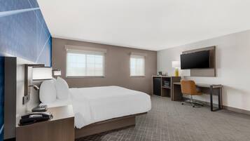 A hotel room with a bed, desk, chair, TV, and a small kitchenette.