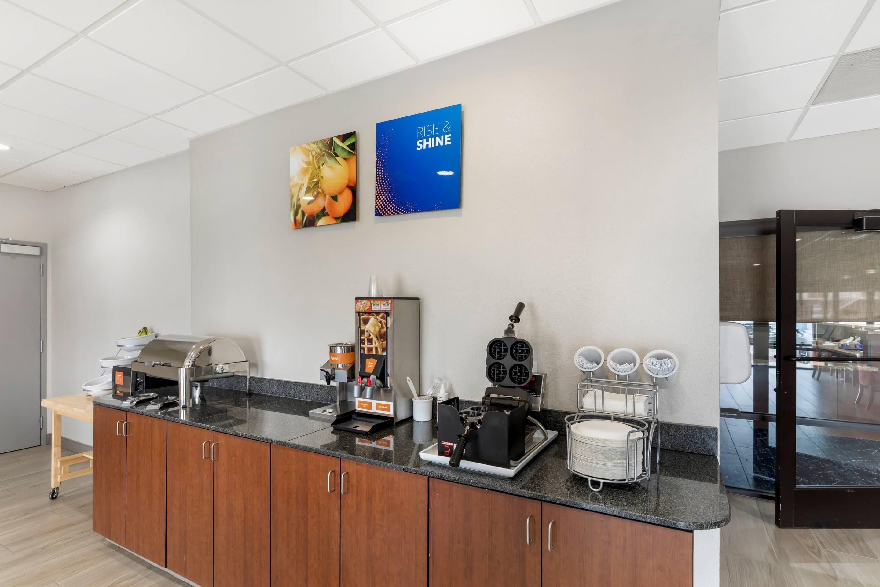 A modern kitchen with a granite countertop, a coffee machine, a waffle maker, and a refrigerator.