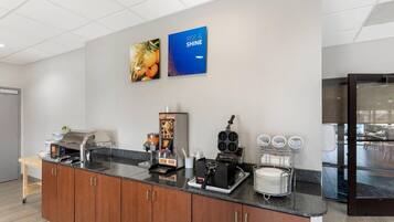 A modern kitchen with a granite countertop, a coffee machine, a waffle maker, and a refrigerator.