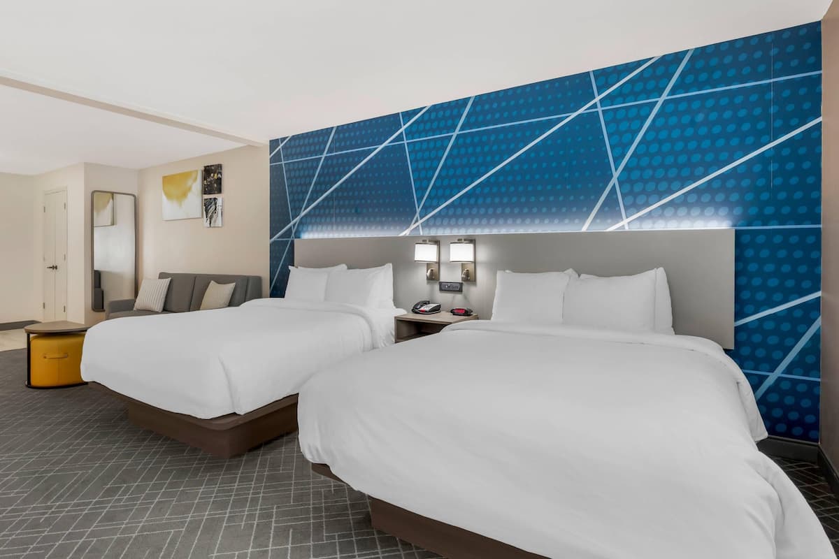 Une chambre d’hôtel avec deux lits, une table de chevet avec un téléphone et une lampe, un miroir et un mur orné d’un motif géométrique.