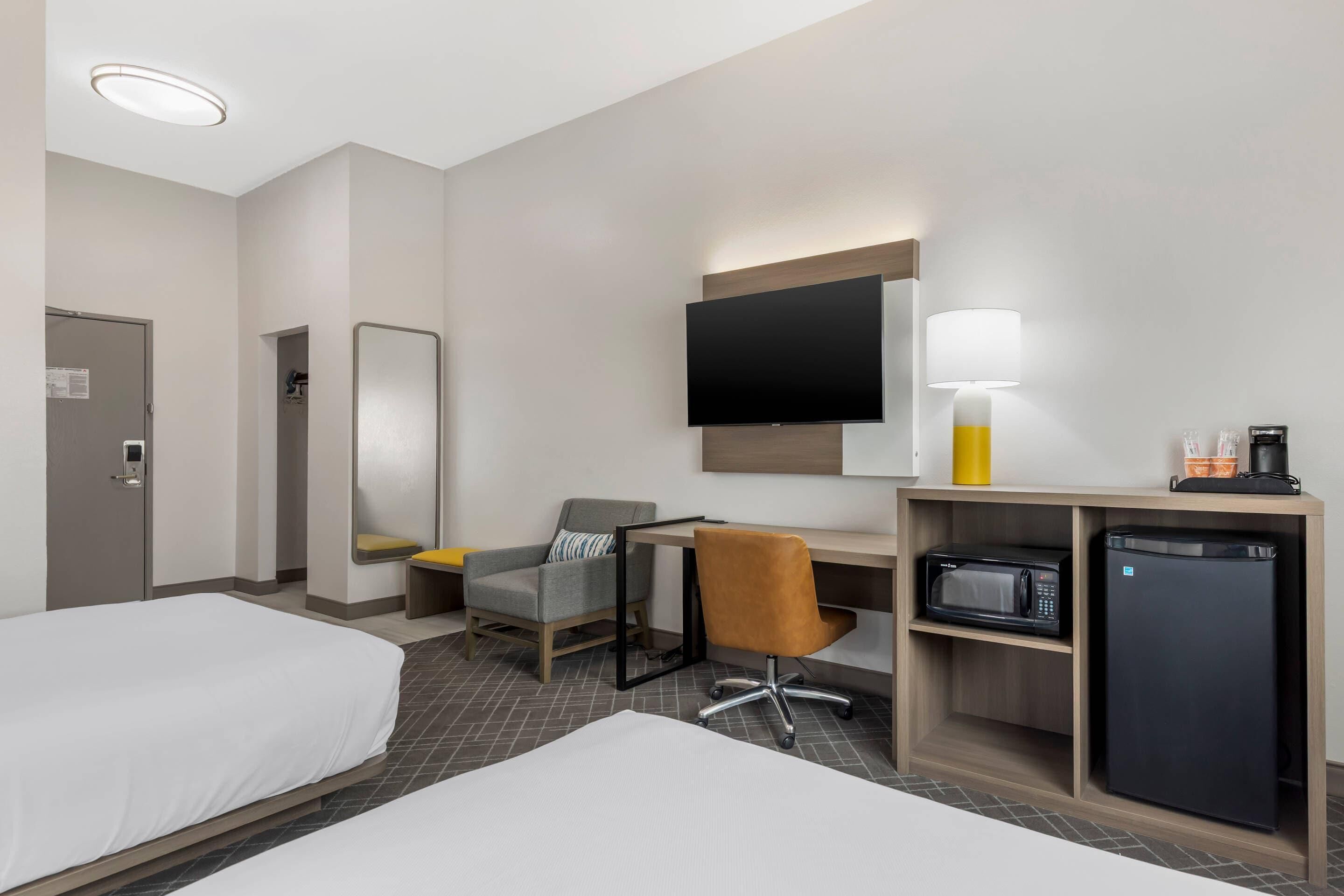 A hotel room with two beds, a desk with a chair, a television, a lamp, a microwave, and a refrigerator.