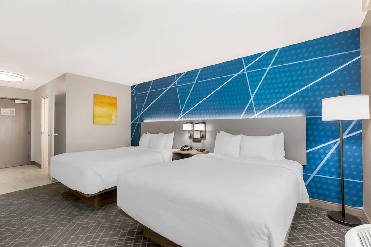 Une chambre d’hôtel avec deux lits, une table de chevet, une lampe et un mur orné d’un motif géométrique.