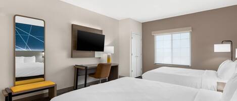 A hotel room with a large bed, a smaller bed, a desk with a chair, a television, and a window with blinds.