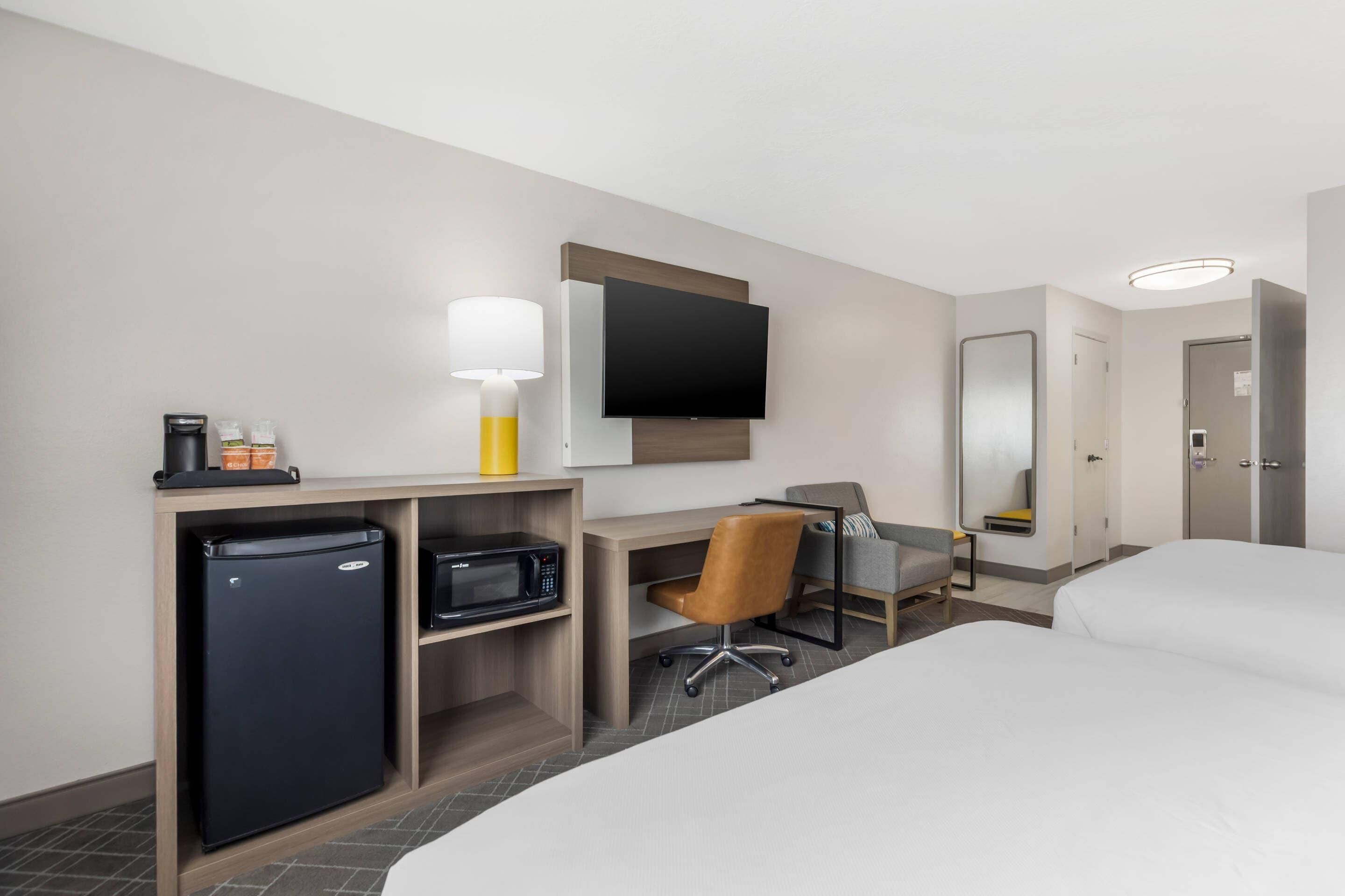 Habitación de hotel con cama, escritorio, silla, televisión, refrigerador y microondas.