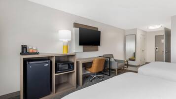 Habitación de hotel con cama, escritorio, silla, televisión, refrigerador y microondas.