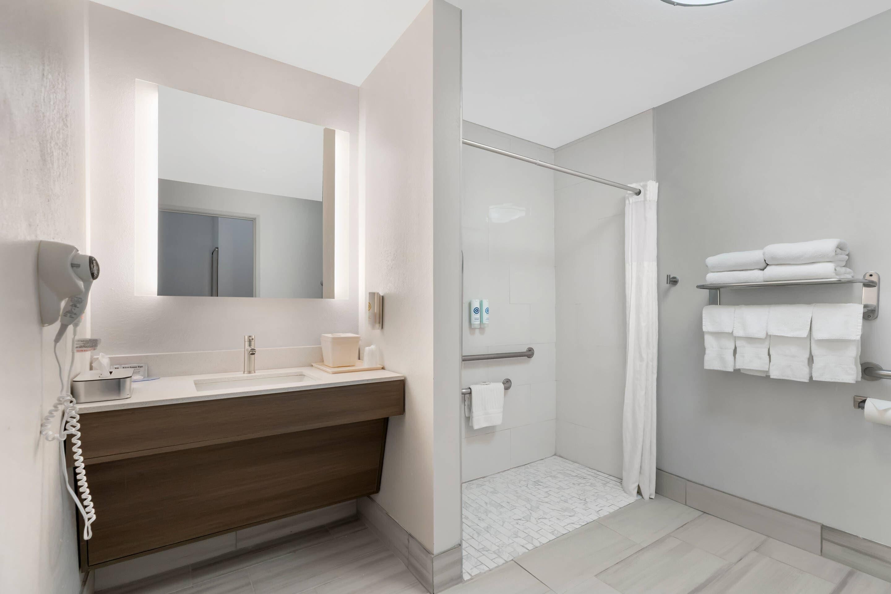A modern bathroom with a wooden vanity, a glass shower enclosure, and neatly folded towels on a rack.