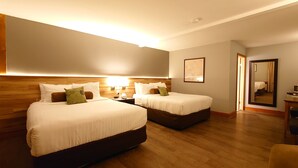 A hotel room with two beds, a wooden headboard, a bedside table with a lamp, a large mirror, and a framed picture on the wall. - Timberland Inn (Kenora)