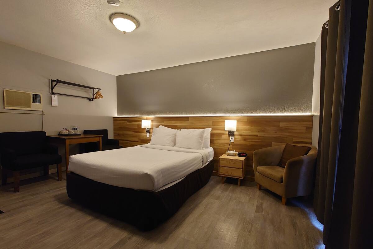 Hotellihuone, jossa on suuri sänky, kaksi yöpöytää, työpöytä, tuoli ja sängynpääty, jossa on sisäänrakennettu valaistus.