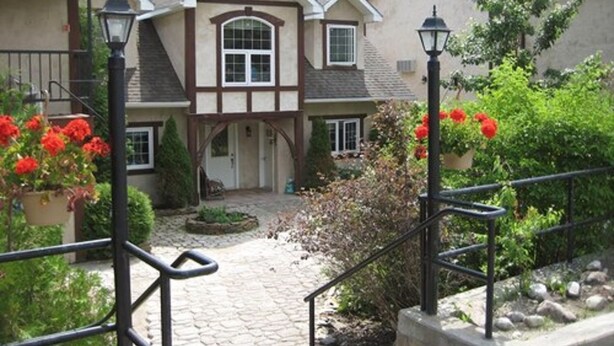 A traditional house with a stone pathway leading to the entrance, surrounded by greenery and red flowers. - Timberland Inn (Kenora)
