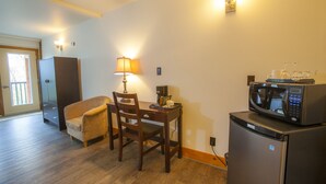 A compact kitchen with a refrigerator, microwave, and a dining area with a chair and table. - Timberland Inn (Kenora)