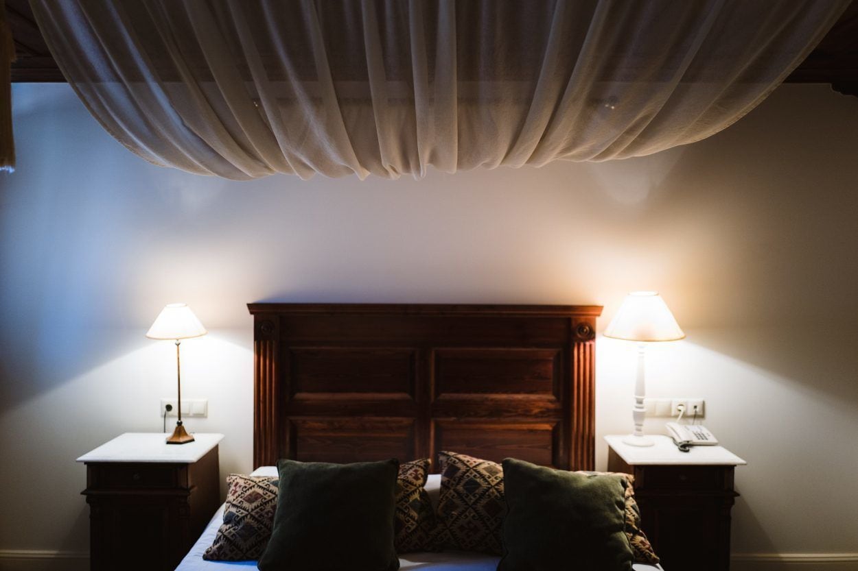 Un dormitorio con cabecera de madera, dos mesitas de noche con lámparas y almohadas estampadas.
