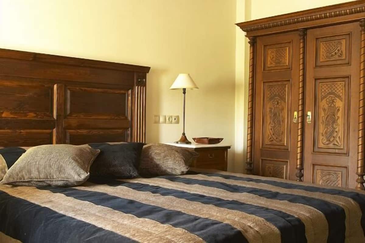 A bed with a striped bedspread, a bedside lamp, and a wooden wardrobe with intricate carvings.