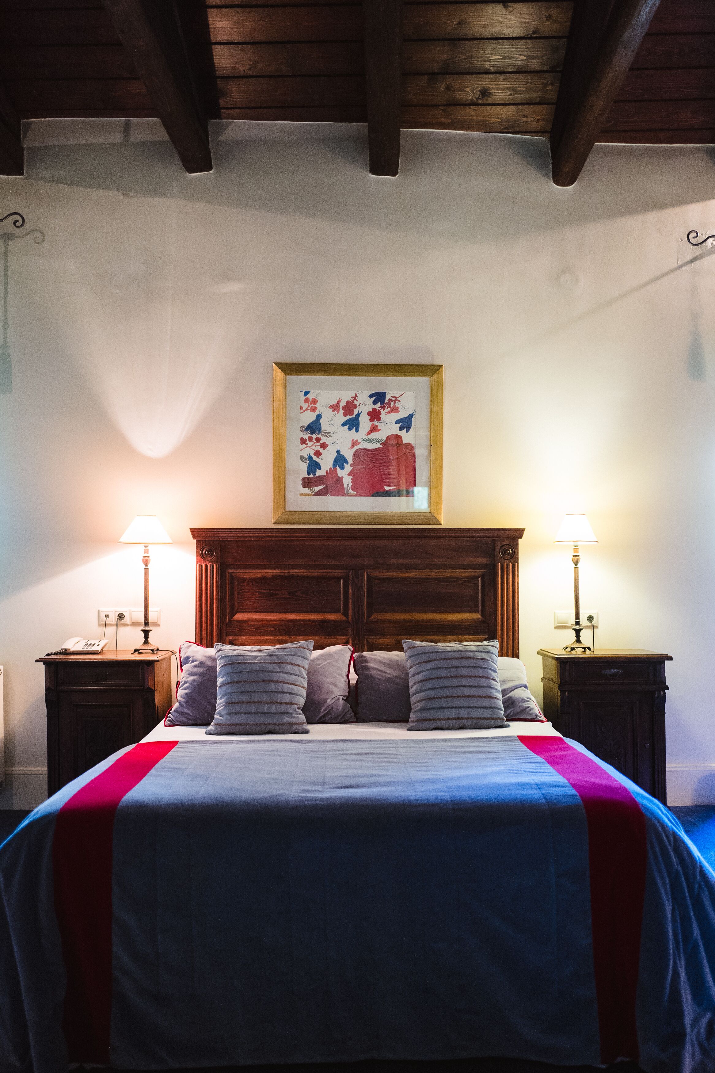 Uma cama com cabeceira de madeira, duas mesas de cabeceira com luminárias e um quadro na parede.