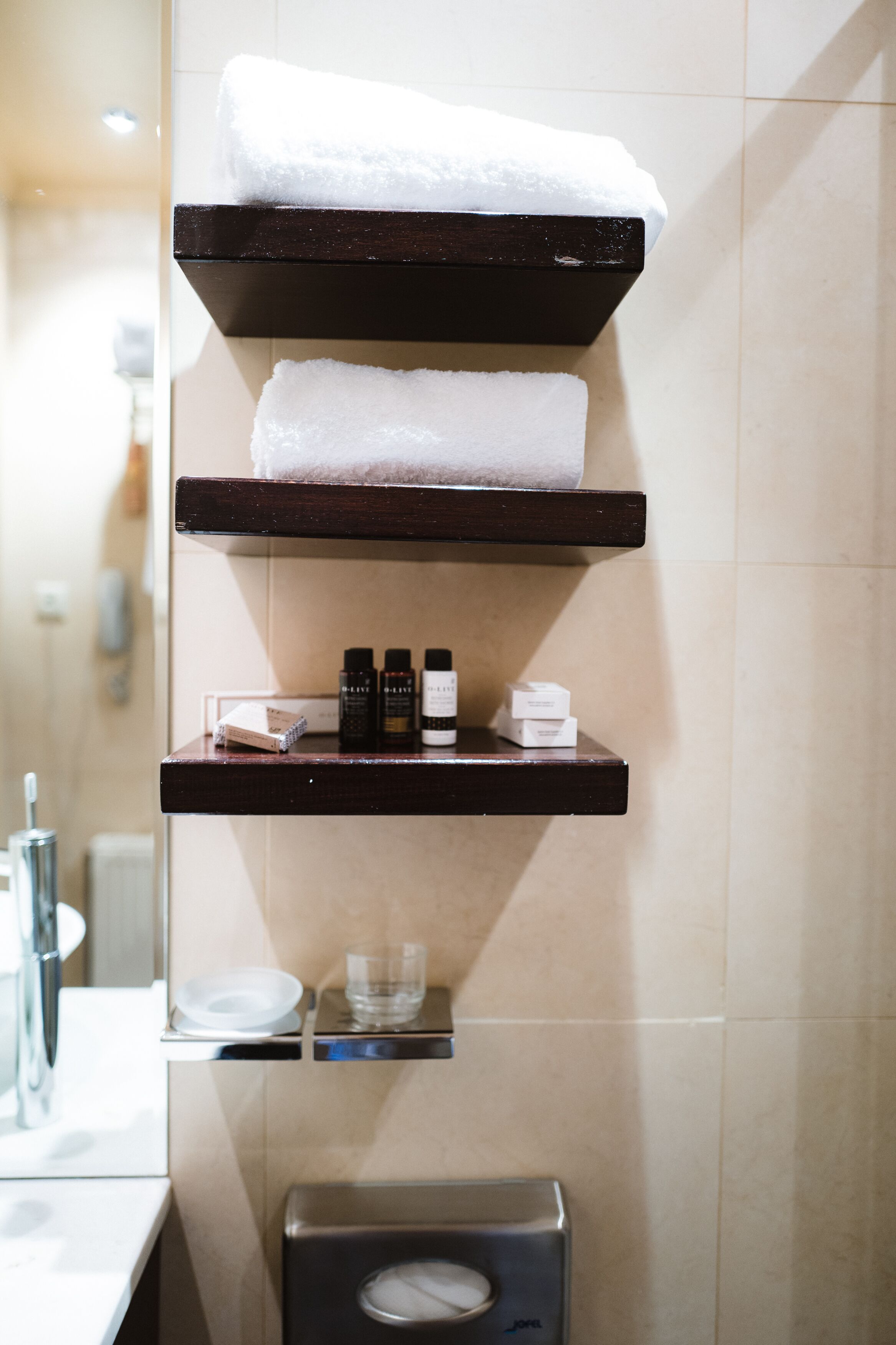 A bathroom with three wooden shelves holding towels and toiletries.