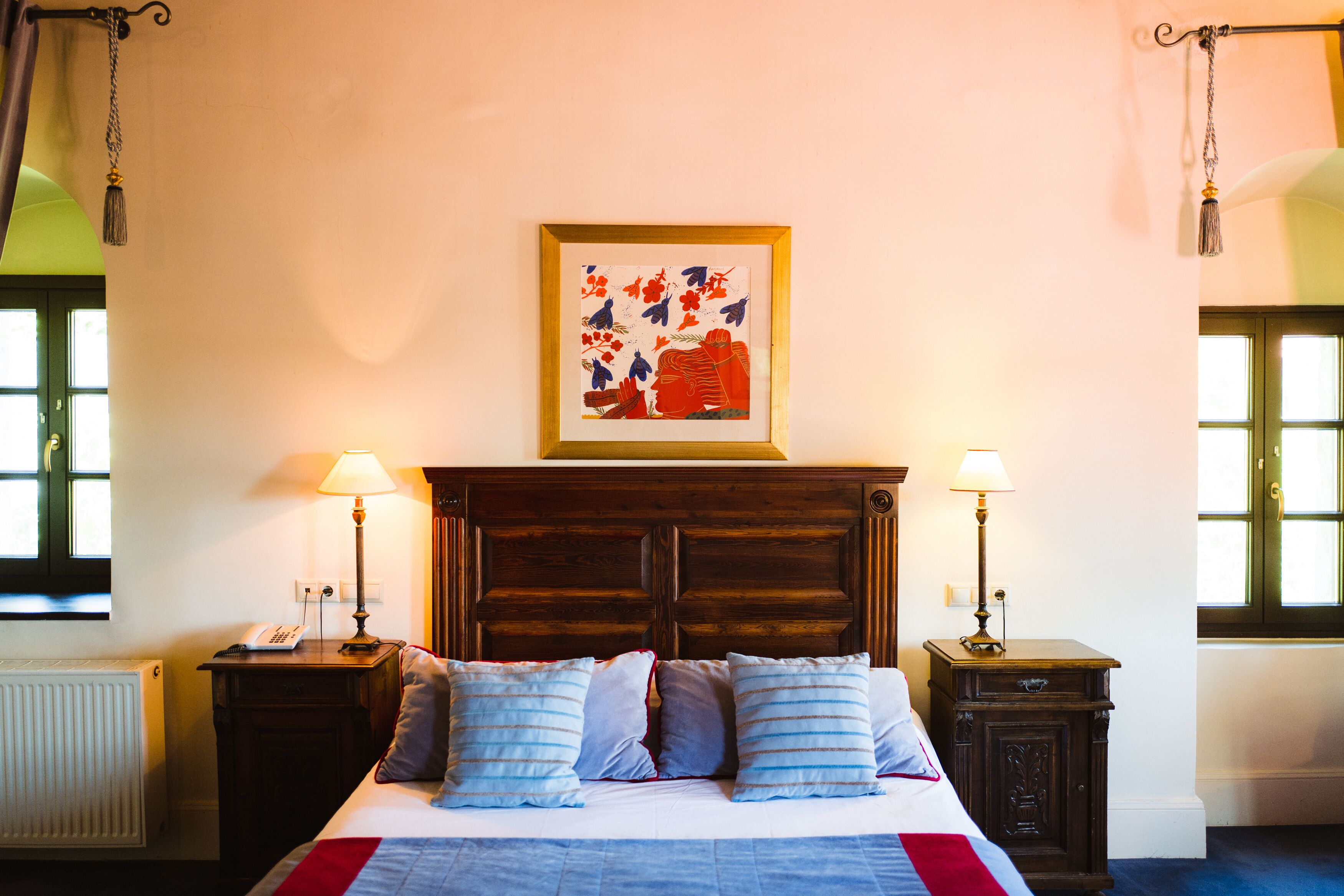 A bedroom with a wooden headboard, two bedside tables with lamps, a bed with blue and white bedding, and a framed artwork on the wall.