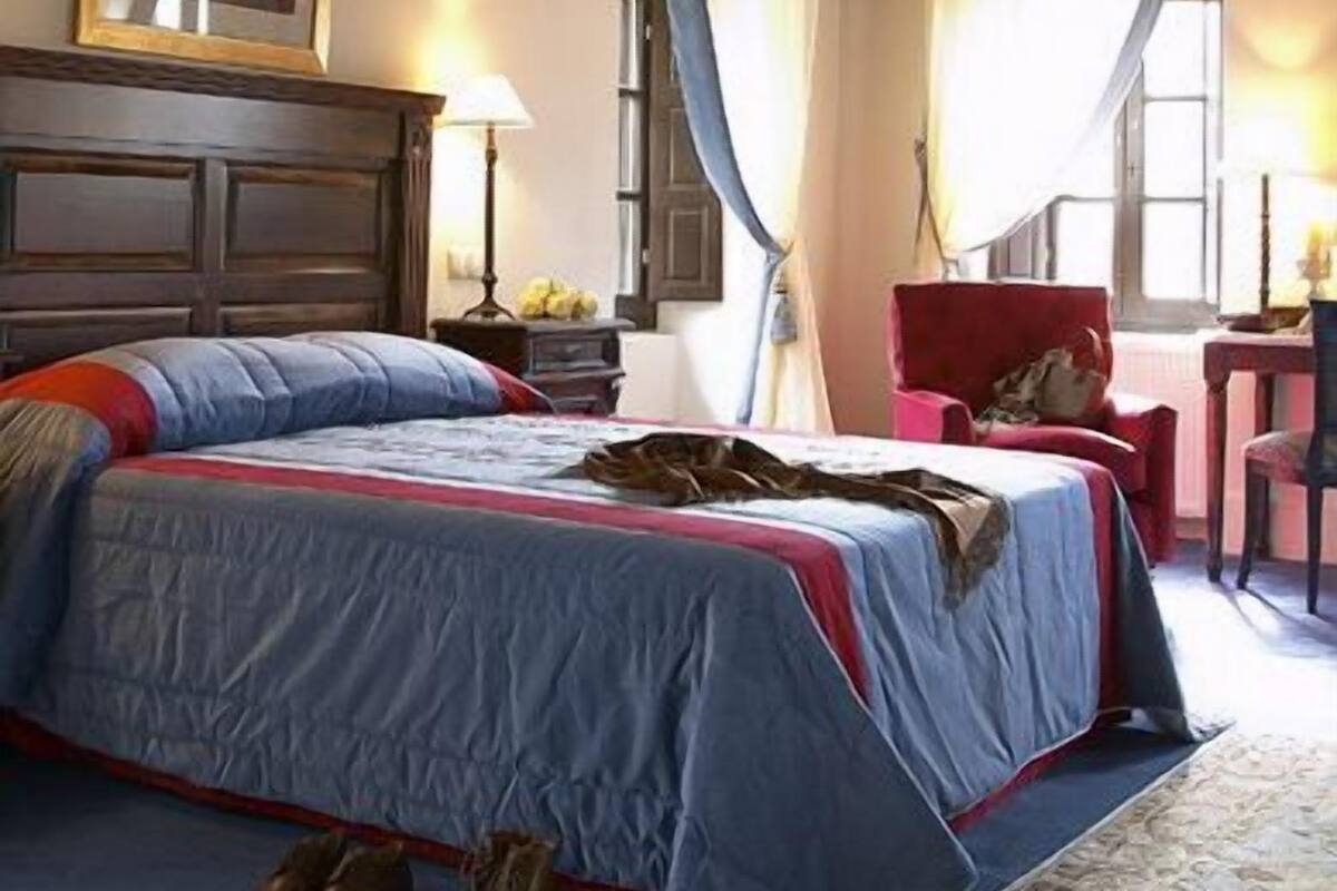 A bedroom with a large bed, a wooden headboard, a framed picture on the wall, and a window with curtains.