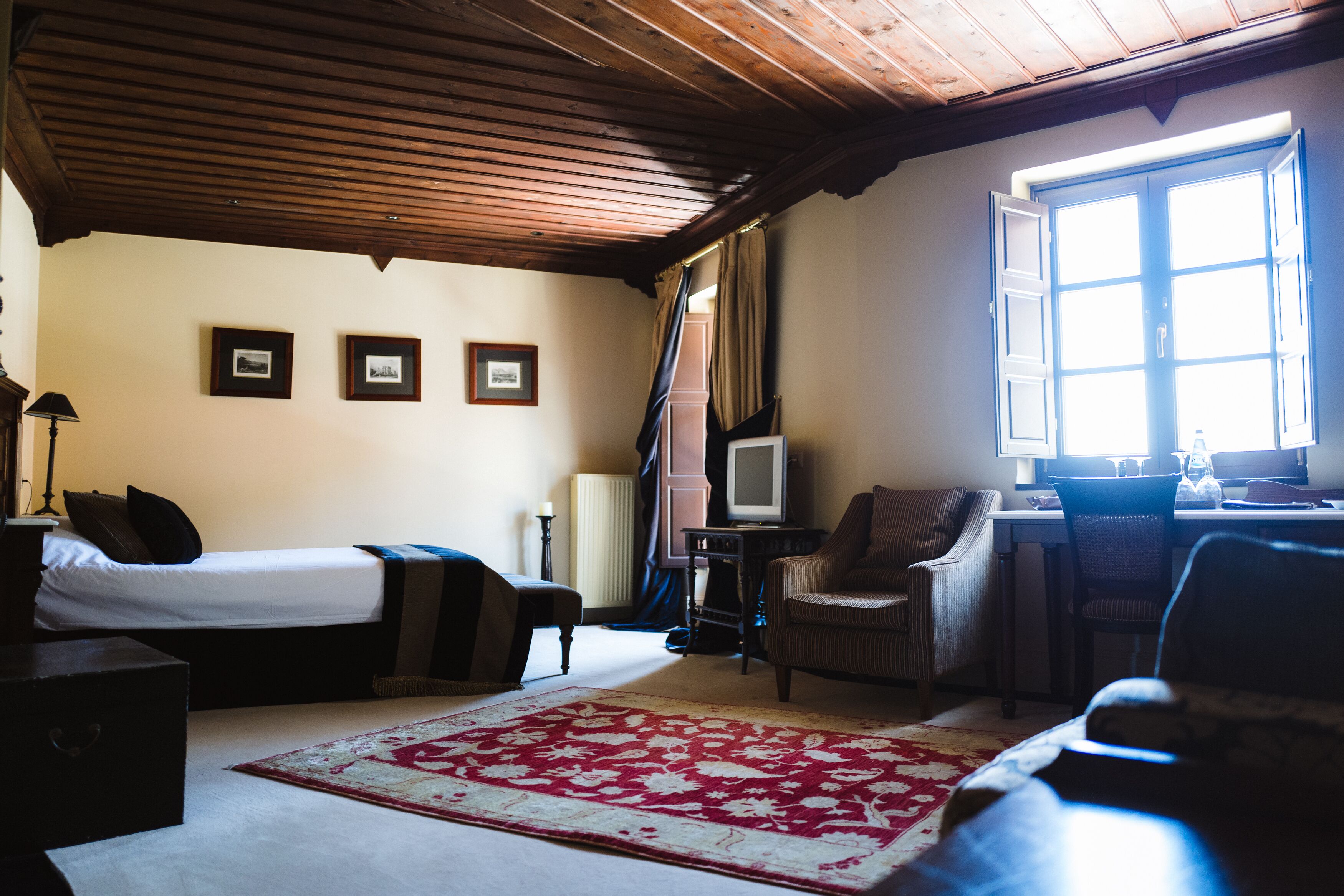 A room with a bed, a desk with a computer, a chair, and a large window with curtains.