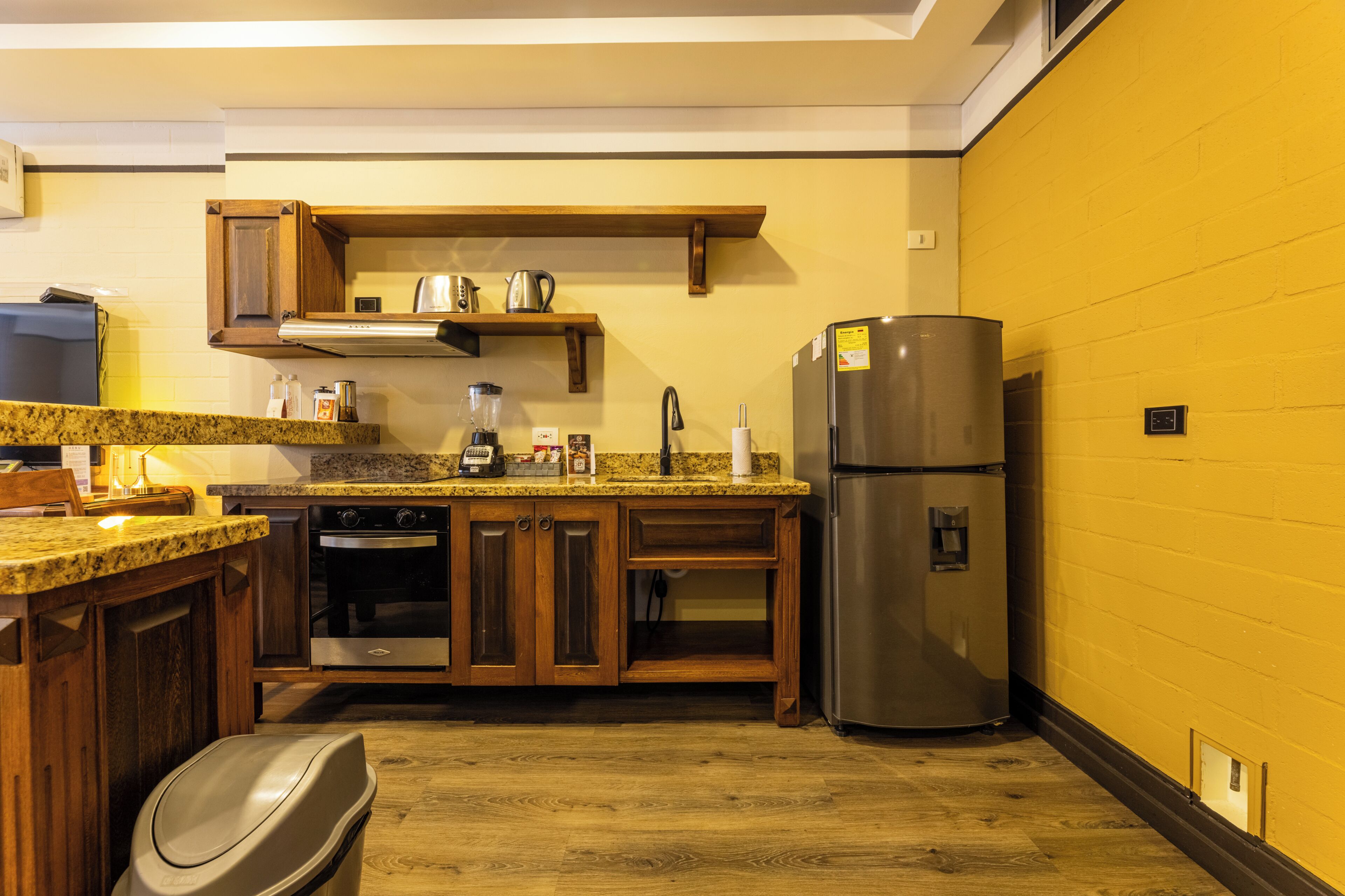 A kitchen with wooden cabinets, a granite countertop, a stainless steel refrigerator, and a built-in oven.