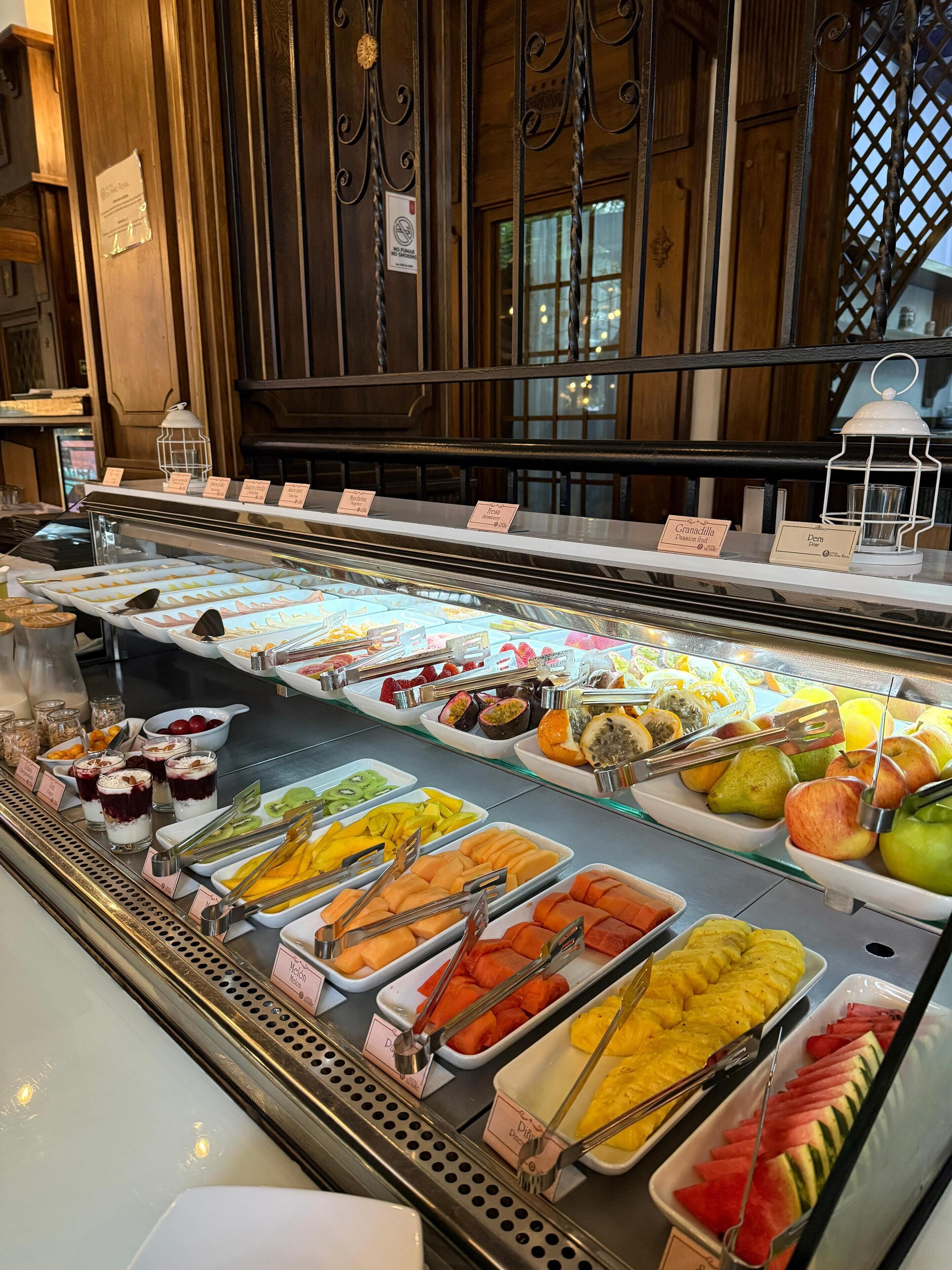 A fruit and dessert display in a bakery with various fruits and desserts neatly arranged in trays.