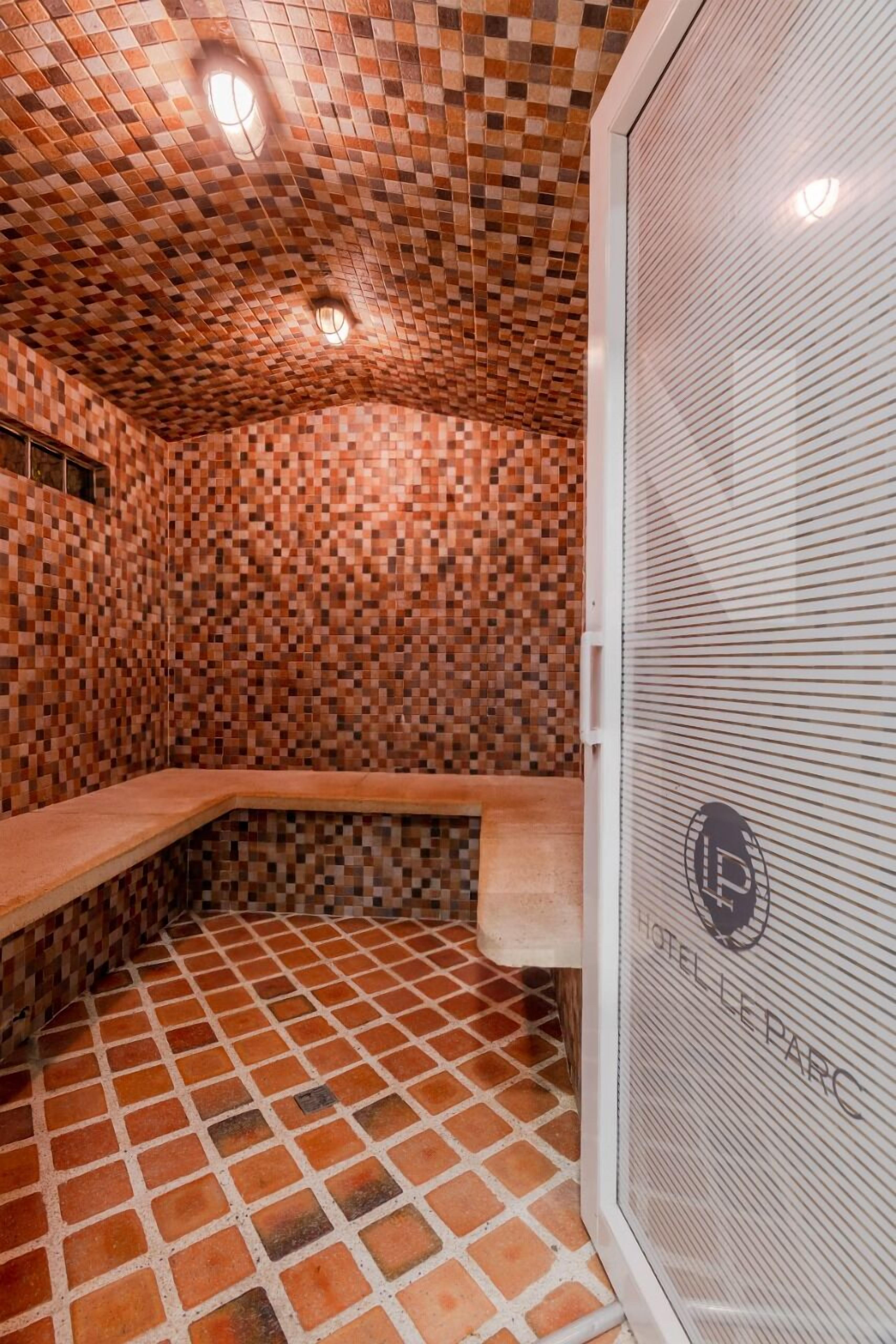 A sauna with checkered tile walls and floor, a bench, and a glass door with a logo.