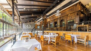 A restaurant with wooden tables and chairs, a bar area, and large windows.
