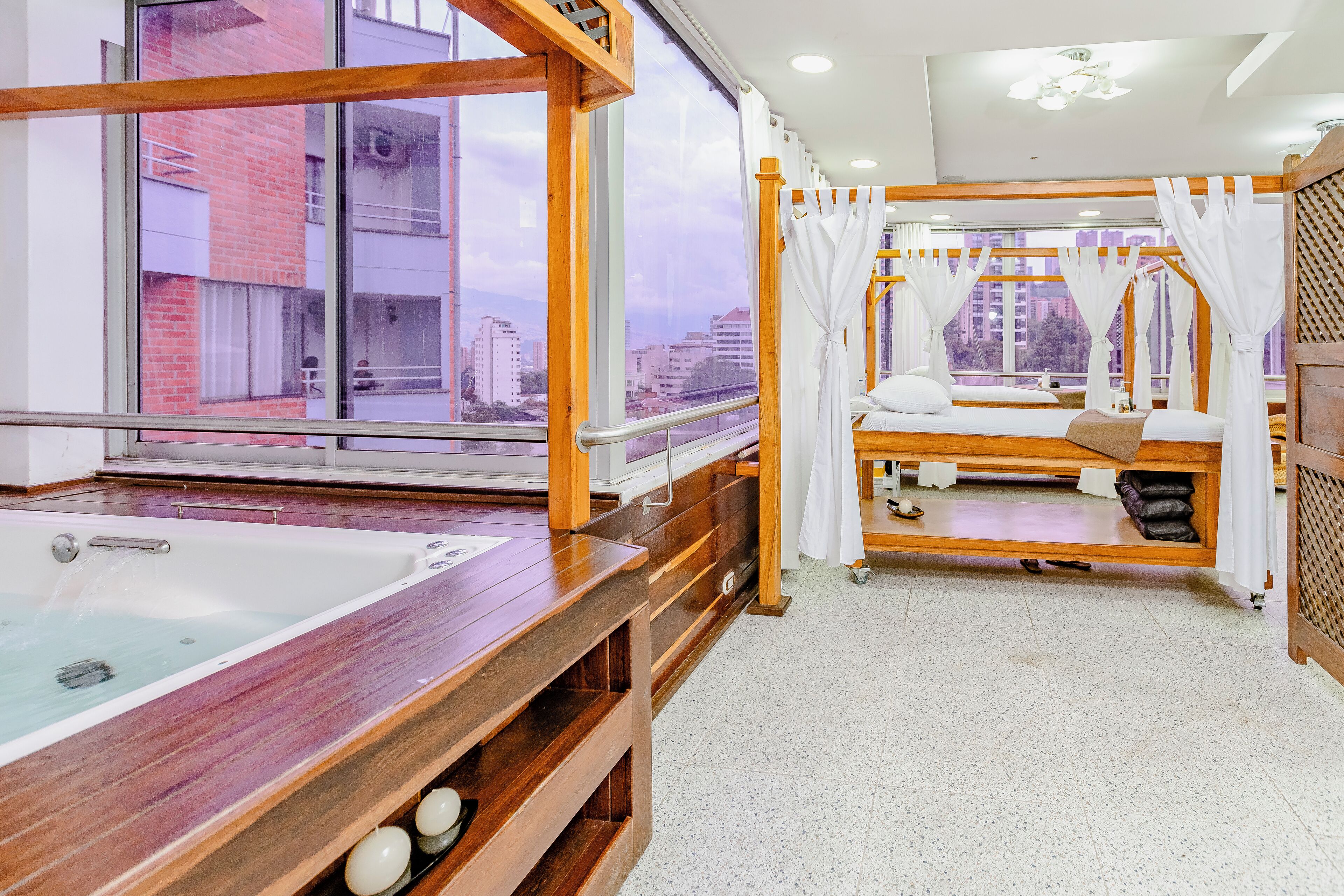 A hotel room with a large window, a bathtub, a bed with a canopy, and a view of the cityscape.