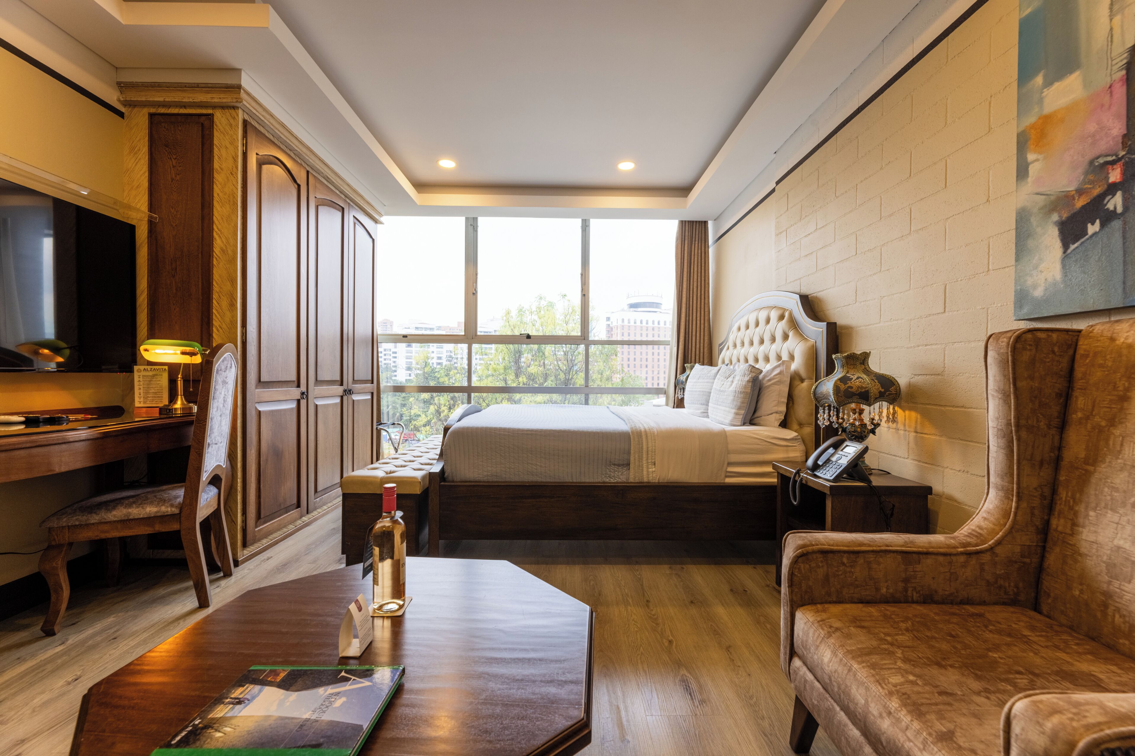 A hotel room with a bed, a desk, a chair, a sofa, a television, and a window with a city view.