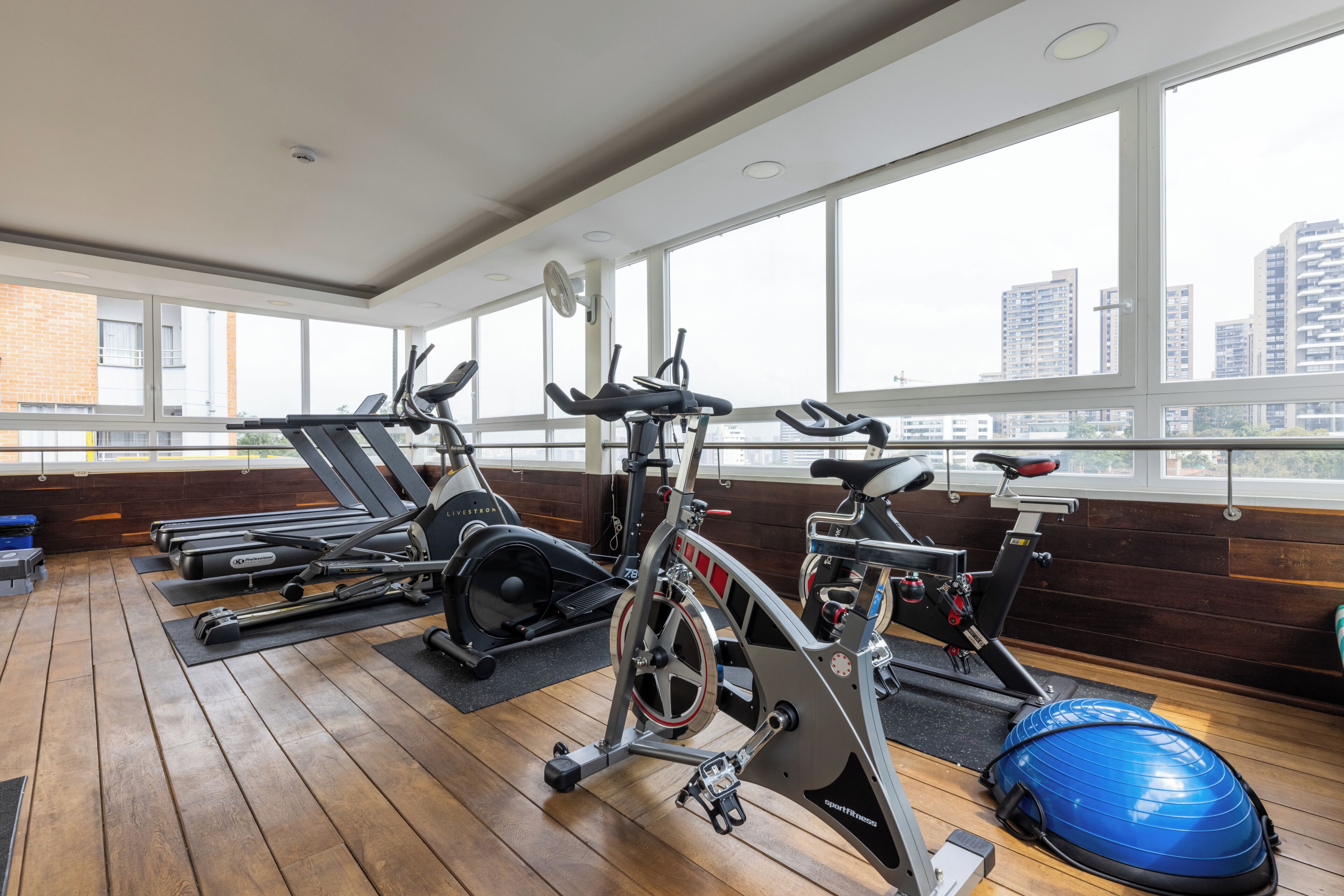 A gym with exercise equipment, large windows, and a view of buildings.