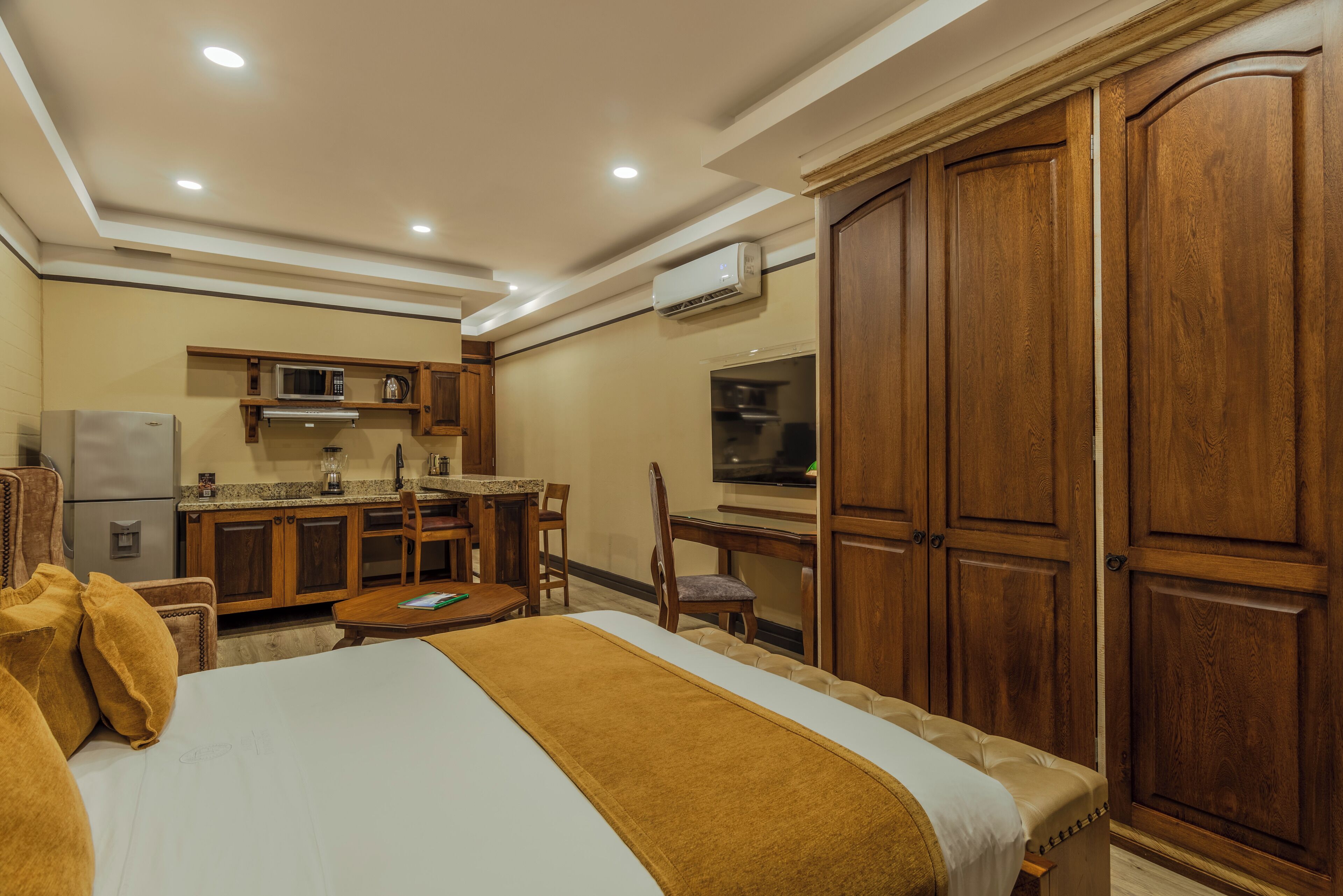 A hotel room with a bed, a desk, a chair, a microwave, a refrigerator, and wooden cabinets.