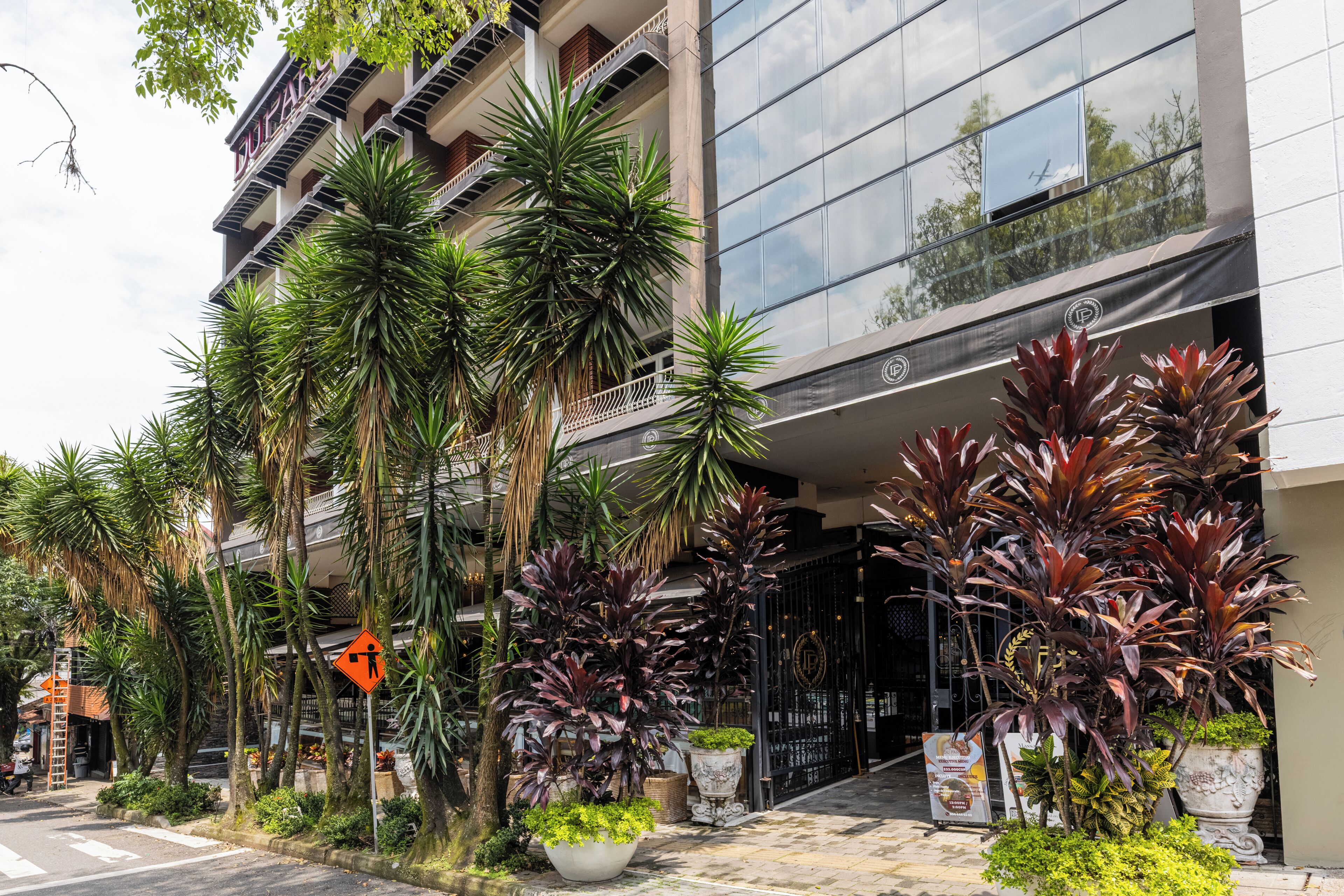 A hotel with a modern facade, multiple balconies, and lush tropical plants.