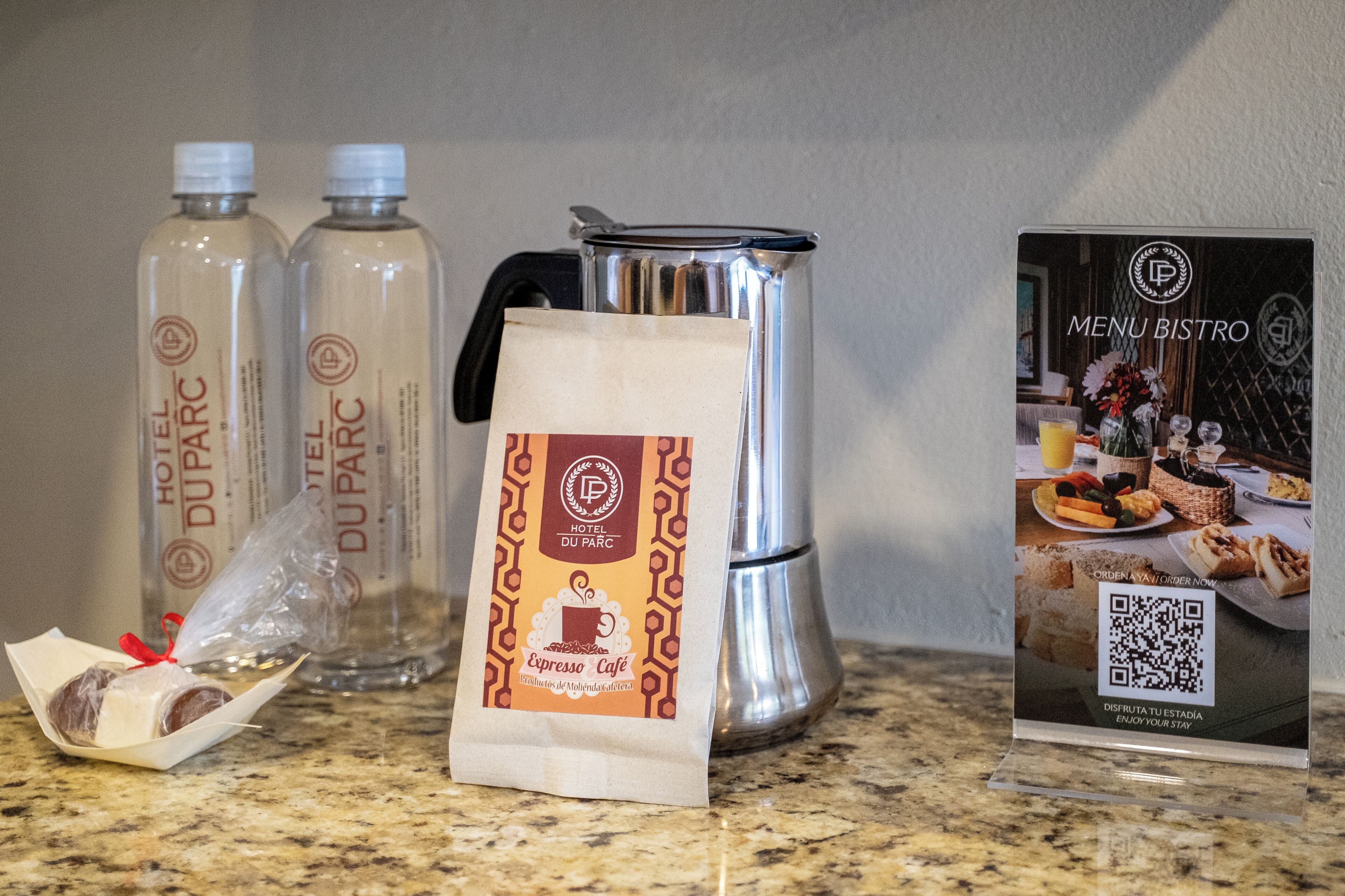 Una cafetera, dos botellas de agua, una bolsa de café y un cartel de menú sobre una encimera.
