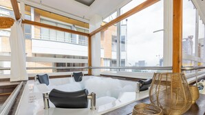 A modern spa area with a large bathtub, wooden flooring, and large windows offering city views.