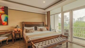 A modern bedroom with a large bed, a wooden desk, and a balcony with a city view.