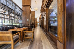 A corridor with wooden furniture, chandeliers, and a glass wall with a view.