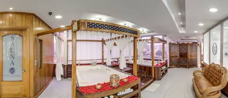 Une salle de spa dotée d’un lit à baldaquin en bois, d’une table de massage et d’un canapé en osier.