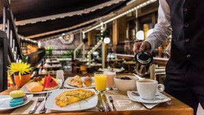A breakfast table with various food items, a cup of coffee, and a waiter pouring coffee.
