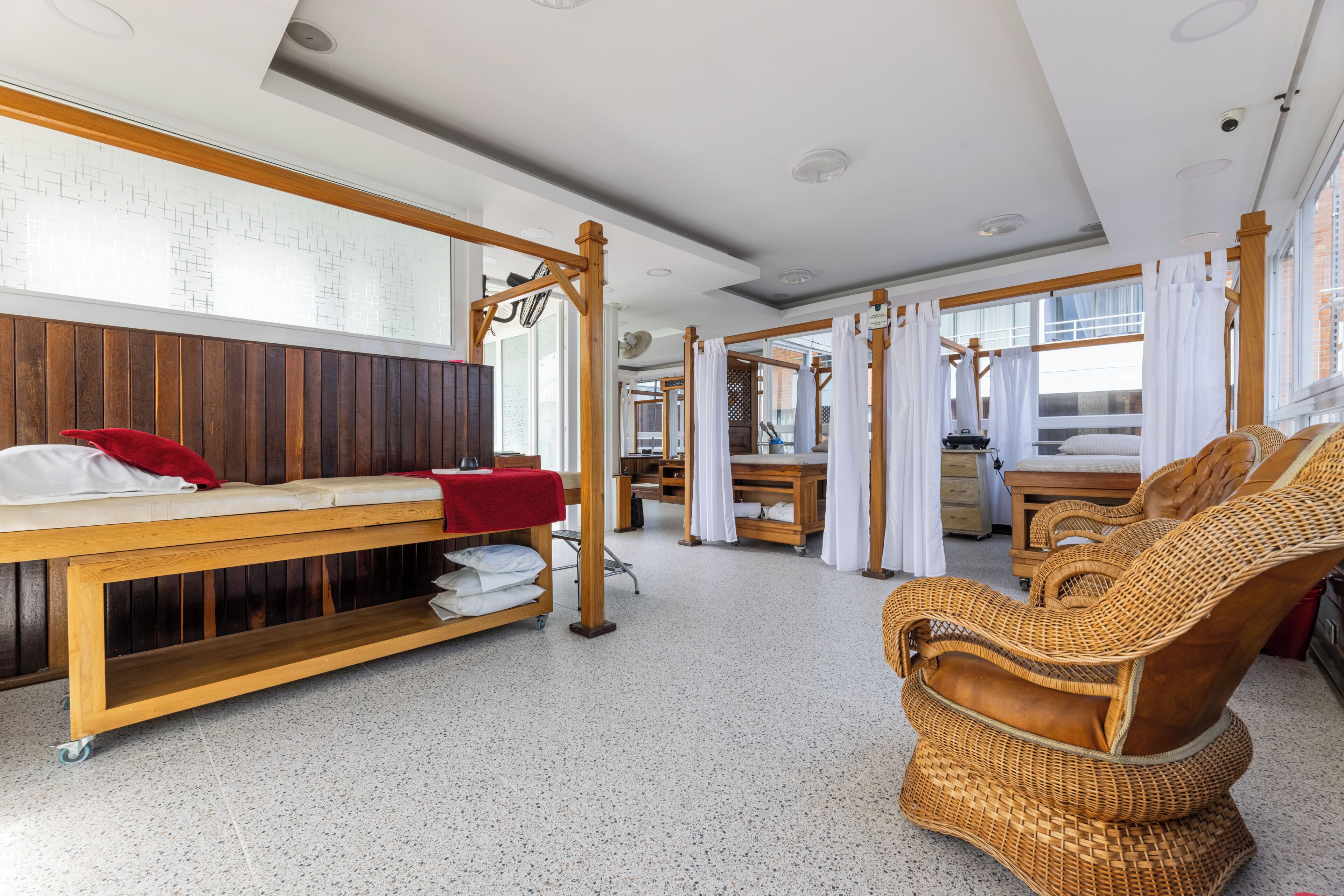Una habitación con un banco de madera, una silla de mimbre y una cama con sábanas blancas.