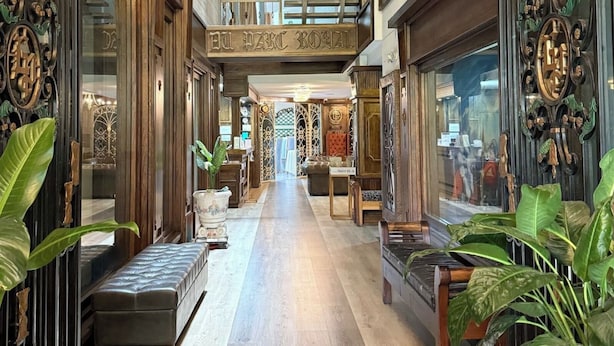 A spacious corridor with wooden paneling, large potted plants, and a central seating area.