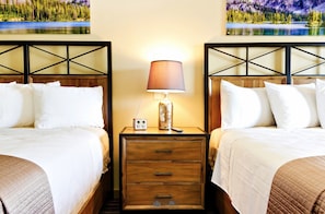 A hotel room with two beds, a nightstand with a lamp, and a painting of a lake. - Blue Lakes Inn & Extended Stay (Twin Falls)