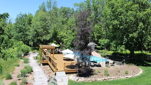 A wooden deck with a pool, surrounded by a garden and a forested area. - The Nutmeg Inn (Meredith)