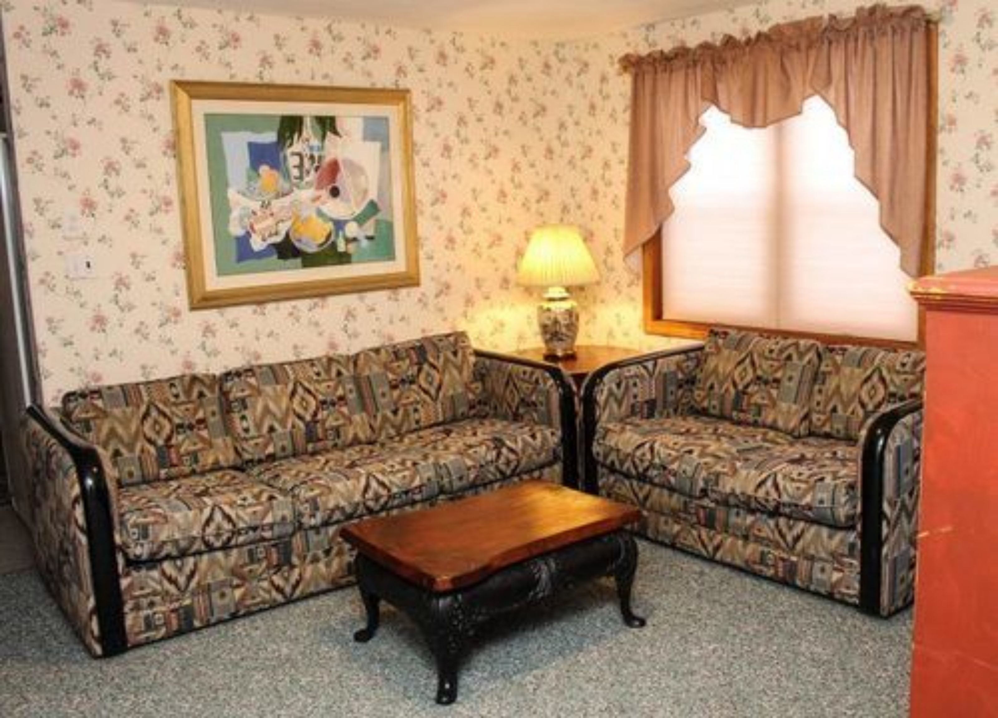 Una sala de estar con dos sofás estampados, una mesa de centro de madera, un cuadro enmarcado en la pared y una lámpara sobre una mesita auxiliar.