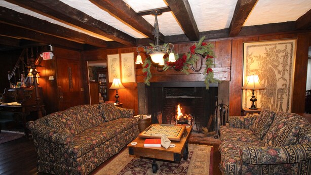 A cozy living room with two patterned sofas, a coffee table with a book, a fireplace, and a Christmas wreath. - The Nutmeg Inn (Meredith)