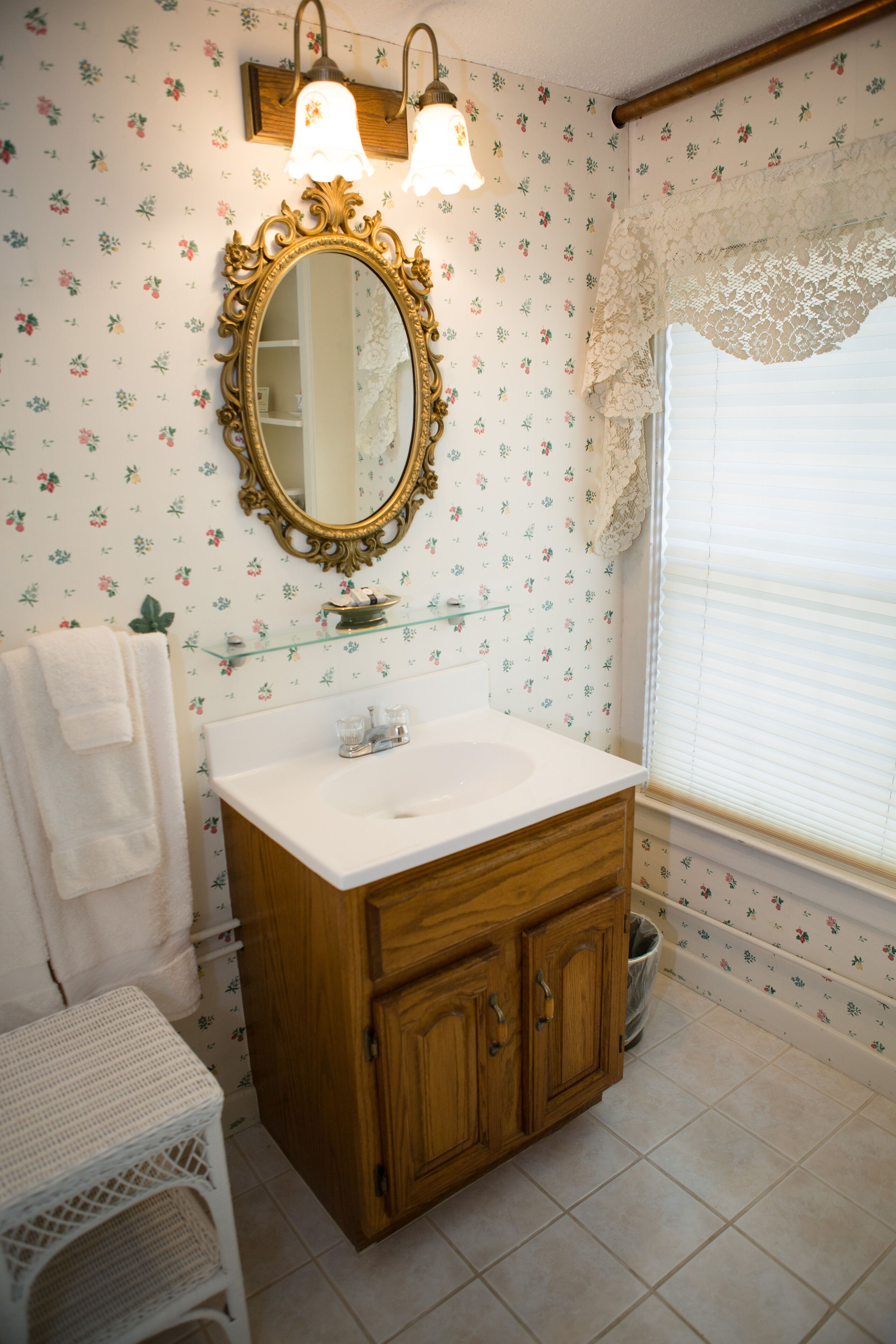 A bathroom with a wooden vanity, a white sink, a mirror with an ornate frame, and floral wallpaper.